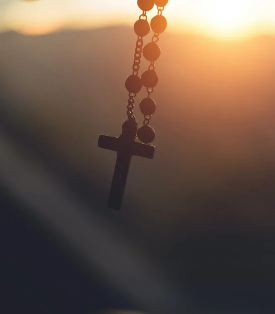 Rosary hanging and dangling in slight shadow with sun rising in background, tip of Rosary hanging with sunrise in background